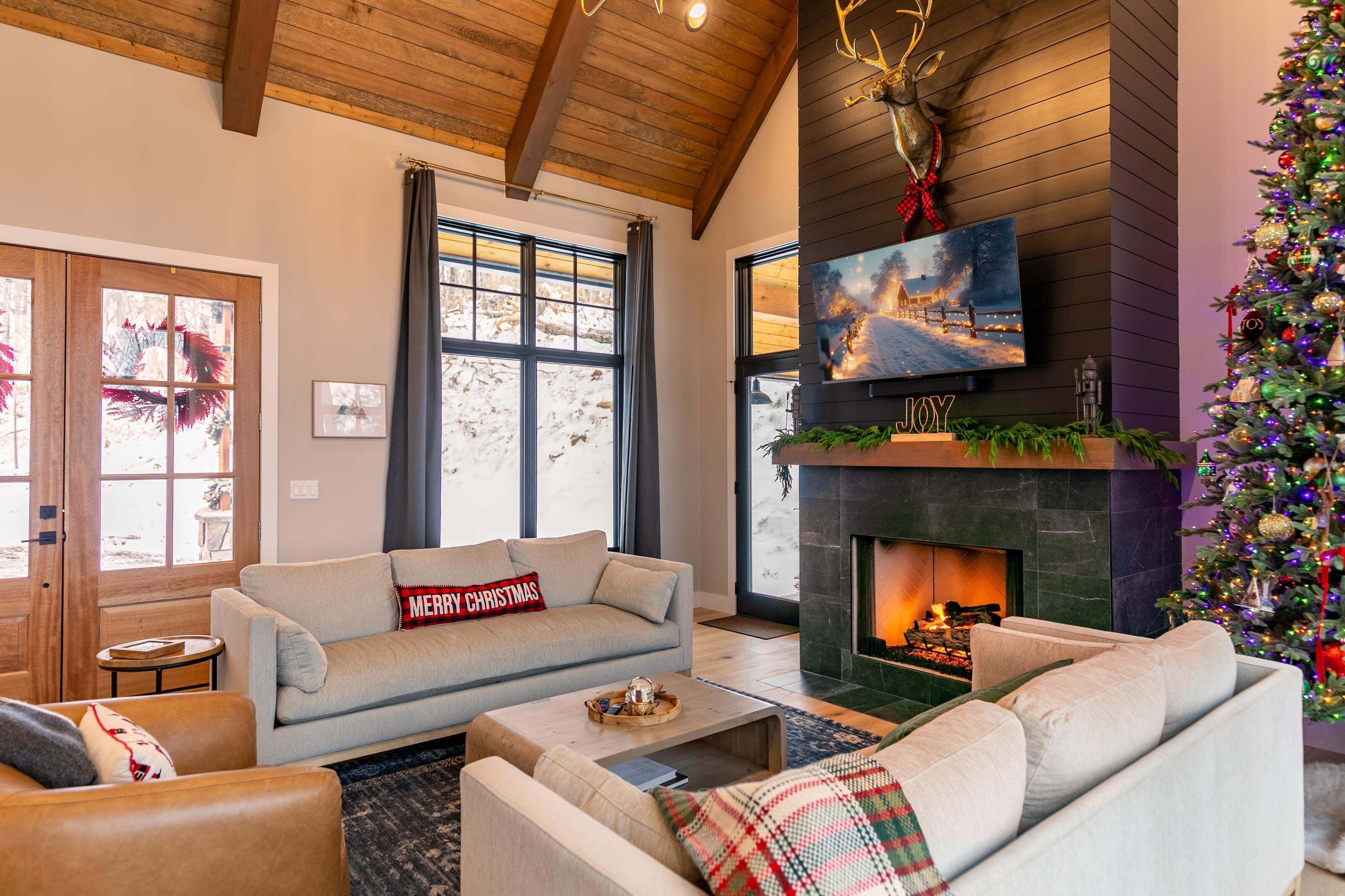 Una sala de estar acogedora con chimenea, un árbol de Navidad y un sofá con un cojín que dice 'Merry Christmas'.