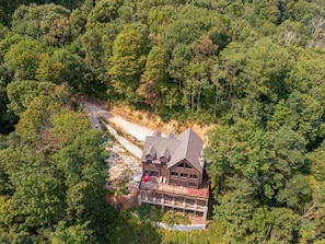 A log cabin with a balcony, surrounded by dense forest.