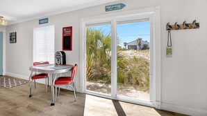 Ett rum med ett matbord, stolar, en radio och utsikt över stranden genom en skjutdörr av glas.