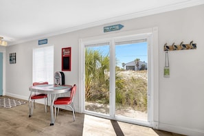 A room with a dining table, chairs, a radio, and a view of the beach through a sliding glass door. - Bristol Breeze - Pet Friendly 2-minute Walk to Beach Ground-floo (Panama City Beach)