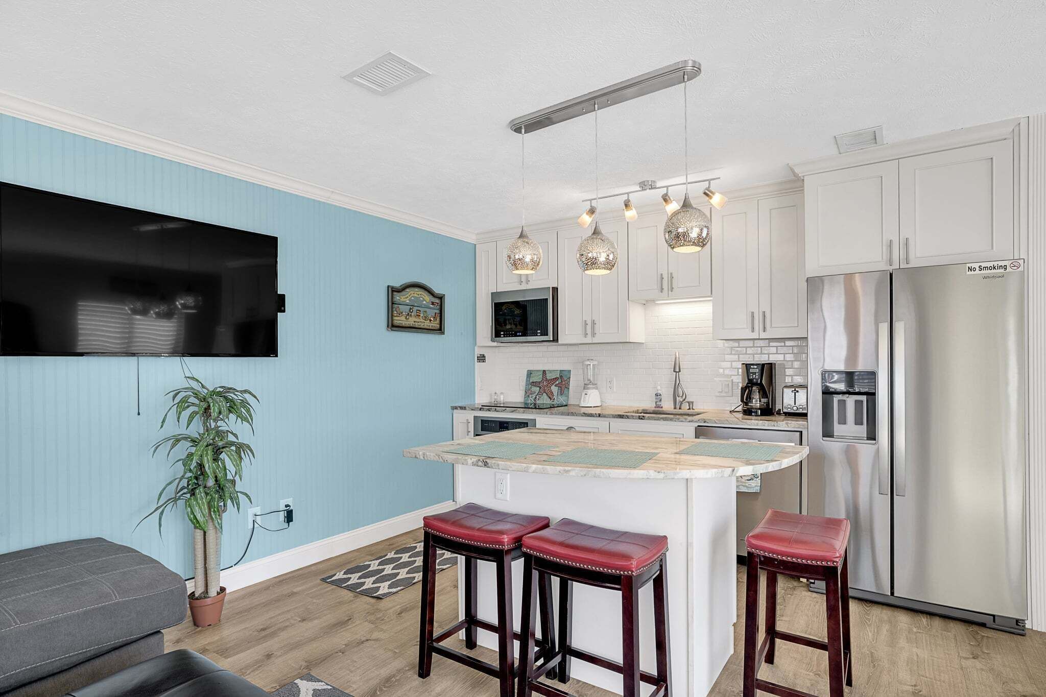 Una cocina moderna con armarios blancos, un refrigerador de acero inoxidable y una zona de bar con taburetes.
