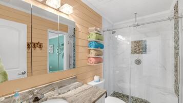 Un baño con lavamanos de mármol, cabina de ducha con mampara de vidrio y espejo con diseño de panel de madera.
