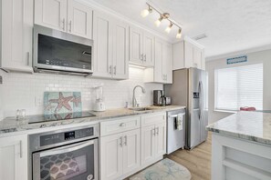 A modern kitchen with white cabinetry, a built-in microwave, stainless steel appliances, and a backsplash with a starfish design. - Bristol Breeze - Pet Friendly 2-minute Walk to Beach Ground-floo (Panama City Beach)