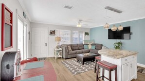 Ett kompakt bostadsutrymme med ett litet kök, en matplats och en sittgrupp med en soffa och en pall.