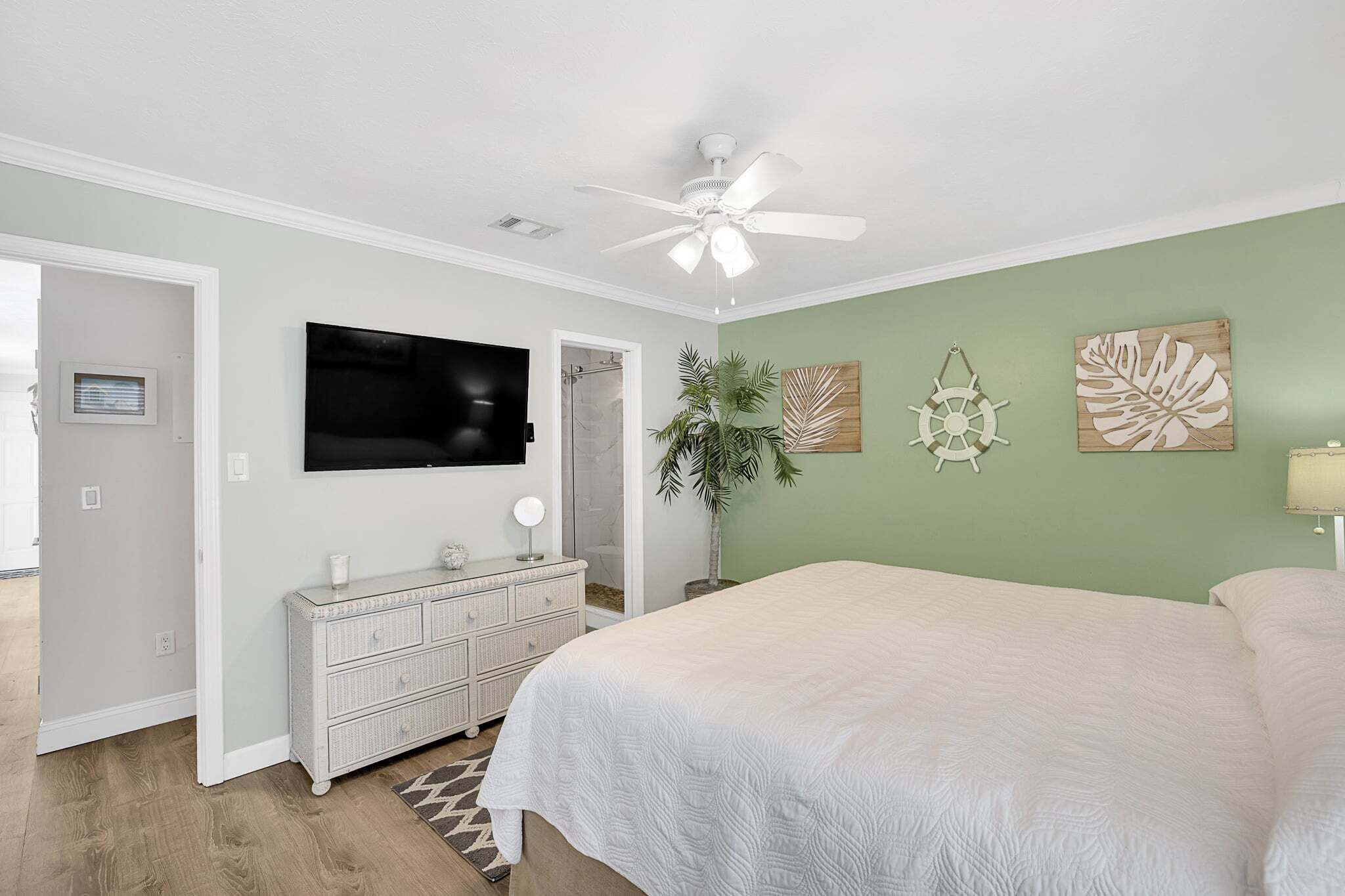 Un dormitorio con una cama, ventilador de techo, televisor, cómoda y decoración en la pared.