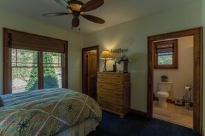 Un dormitorio con cama, cómoda, ventilador de techo, ventanas y vistas al exterior.