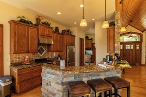 A kitchen with wooden cabinets, a granite countertop, a stone island, and a stainless steel refrigerator.