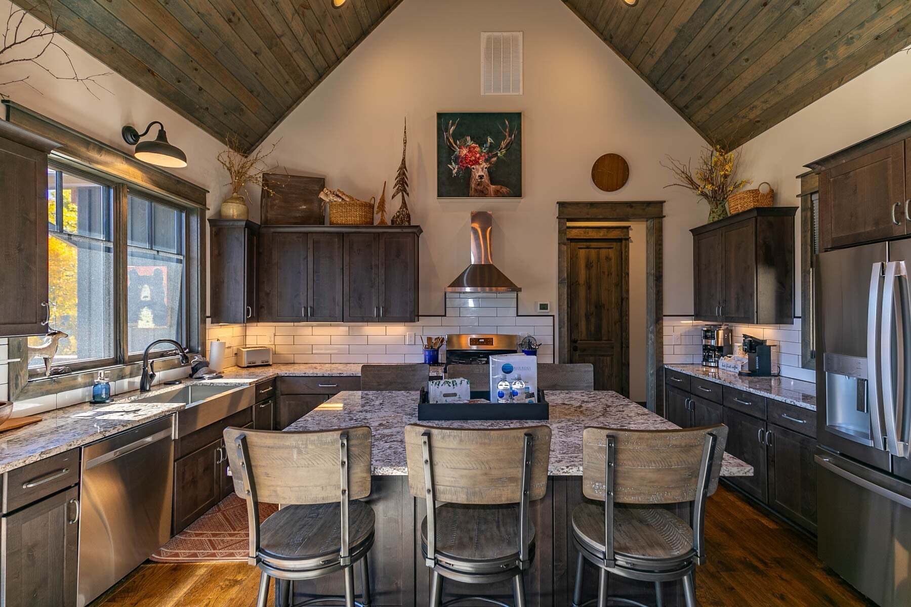 Une cuisine avec des meubles de couleur bois foncé, un îlot central doté de chaises, une cuisinière et une grande fenêtre.
