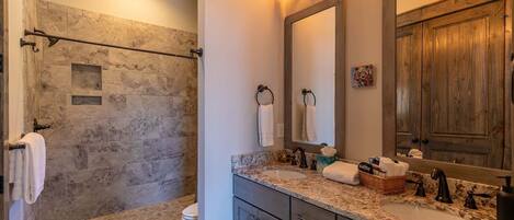 A bathroom with a stone shower, a sink with a mirror, and wooden cabinets.