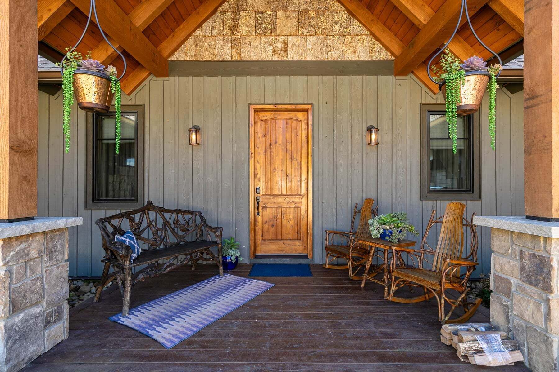 A wooden porch with a bench, rocking chairs, and hanging planters.