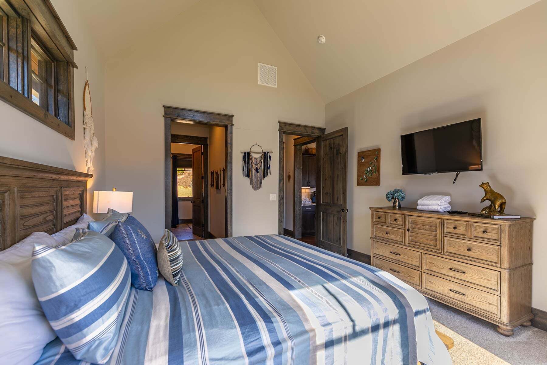 A bedroom with a bed, dresser, TV, and a hallway leading to a kitchen.