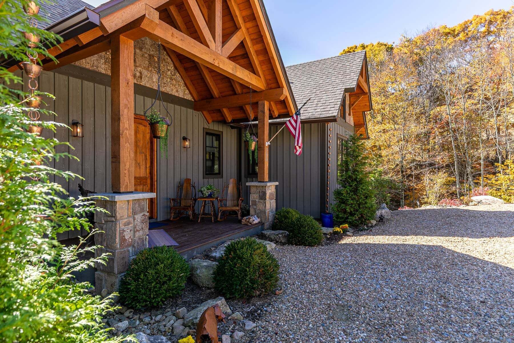 A wooden cabin with a porch, stone steps, and a gravel driveway.