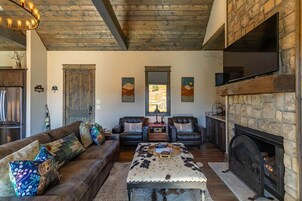 Una sala de estar acogedora con chimenea de piedra, sofás de cuero y techo de madera.