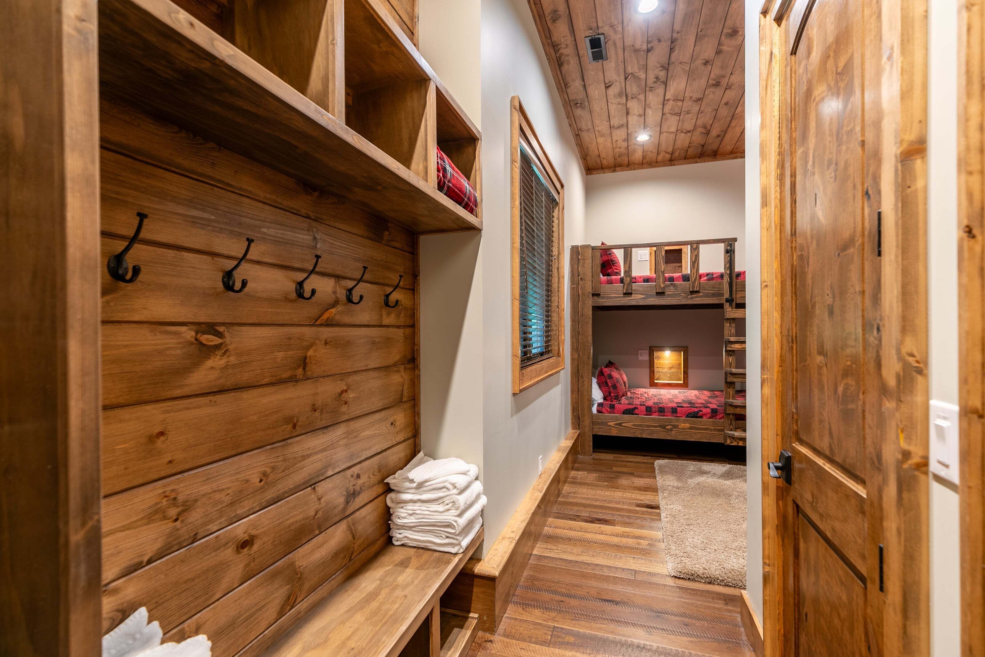 A wooden interior with a bench, hooks, and a bunk bed.