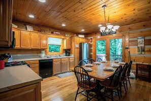 A wooden cabin kitchen with a dining table set for four, wooden cabinets, and a view through the windows. - A Family Tradition (Boone)