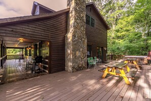 A wooden deck with picnic tables and chairs, a stone pillar, and a covered area with a grill. - A Family Tradition (Boone)