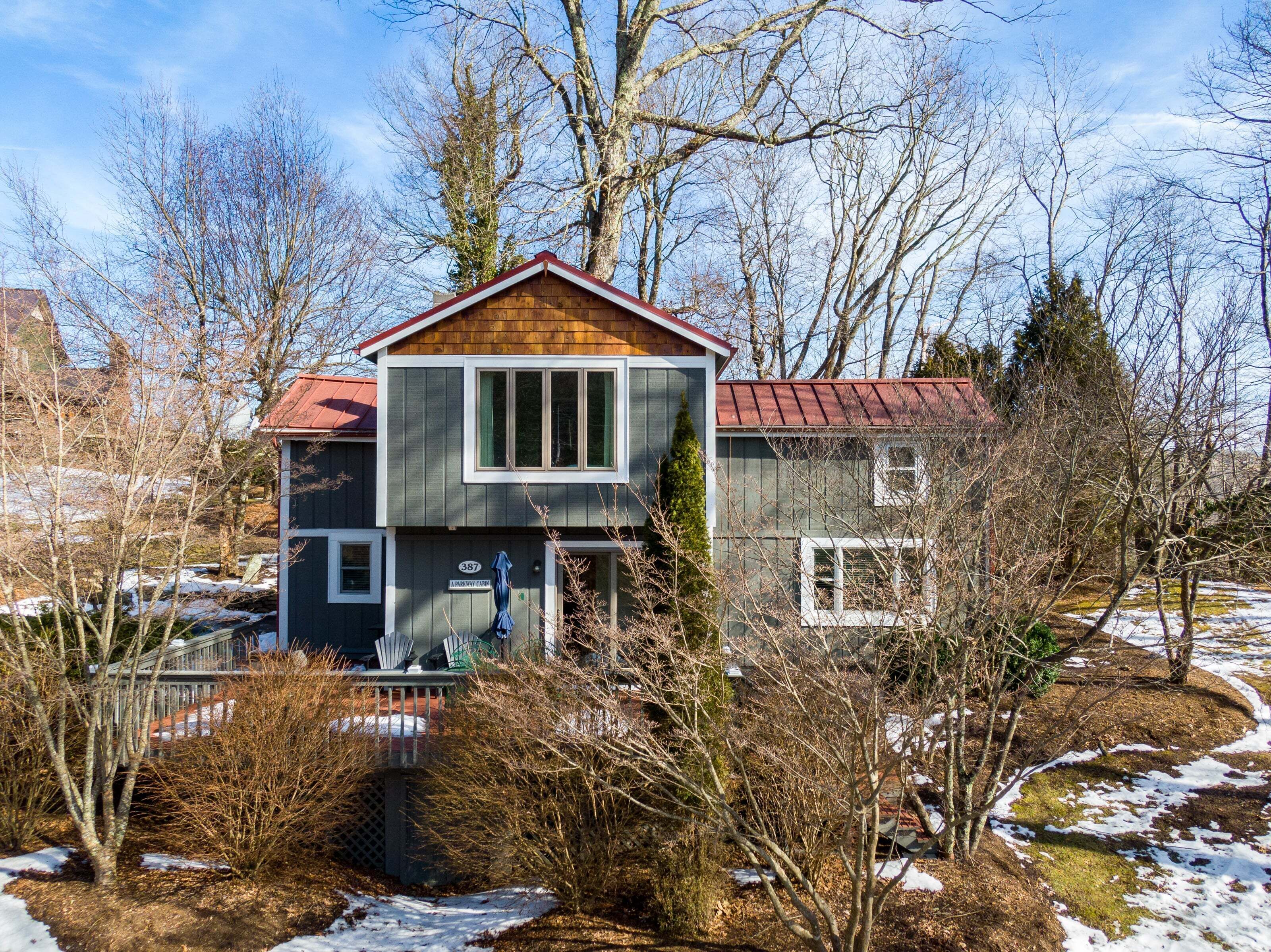 A two-story house with a red roof, a visible number '387', and a fenced yard with snow patches.
