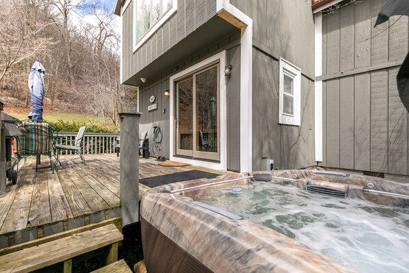Eine Holzterrasse mit Whirlpool, einer überdachten Veranda und einem Haus mit großen Schiebeglasfenstern.