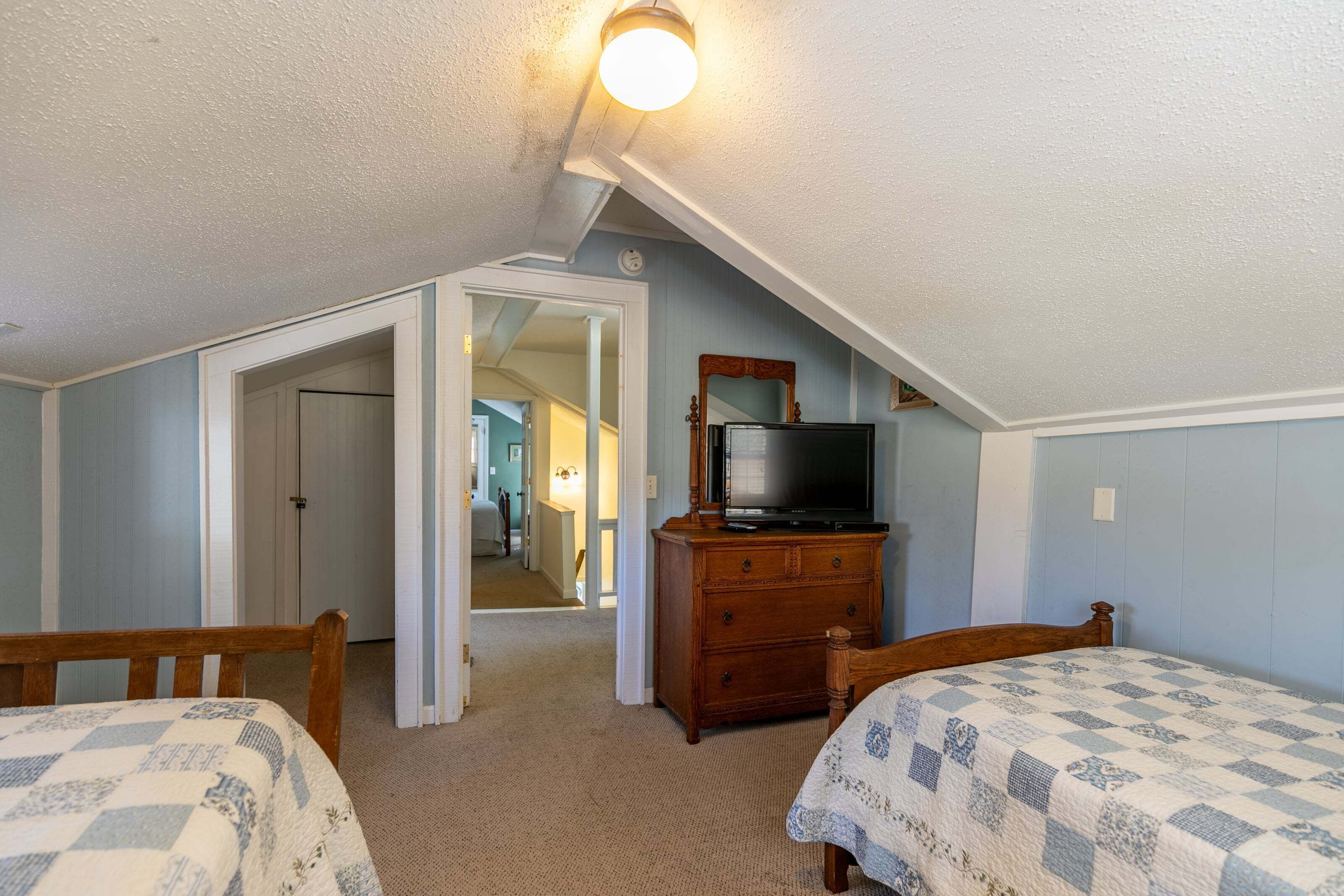 Un dormitorio con dos camas, un aparador, un televisor y una puerta que da a otra habitación.