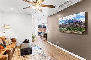 Ein modernes Wohnzimmer mit einem braunen Ledersofa, einem schwarzen Ottomanen und einem großen Gemälde einer Berglandschaft an der Wand.