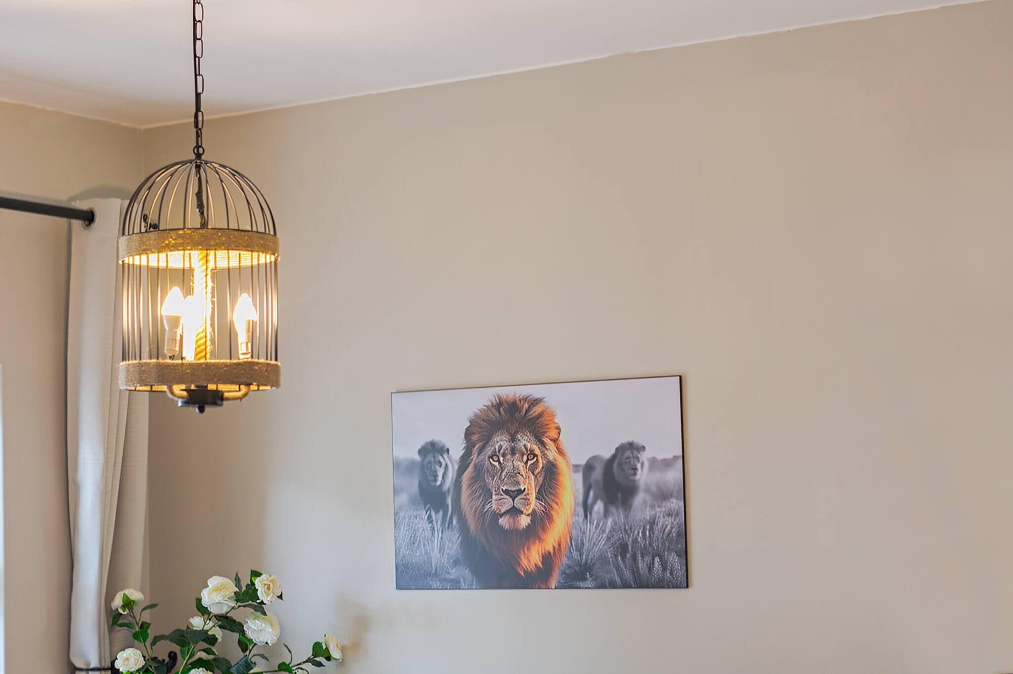 A chandelier with three bulbs, a framed wildlife photograph on the wall, and a white curtain.