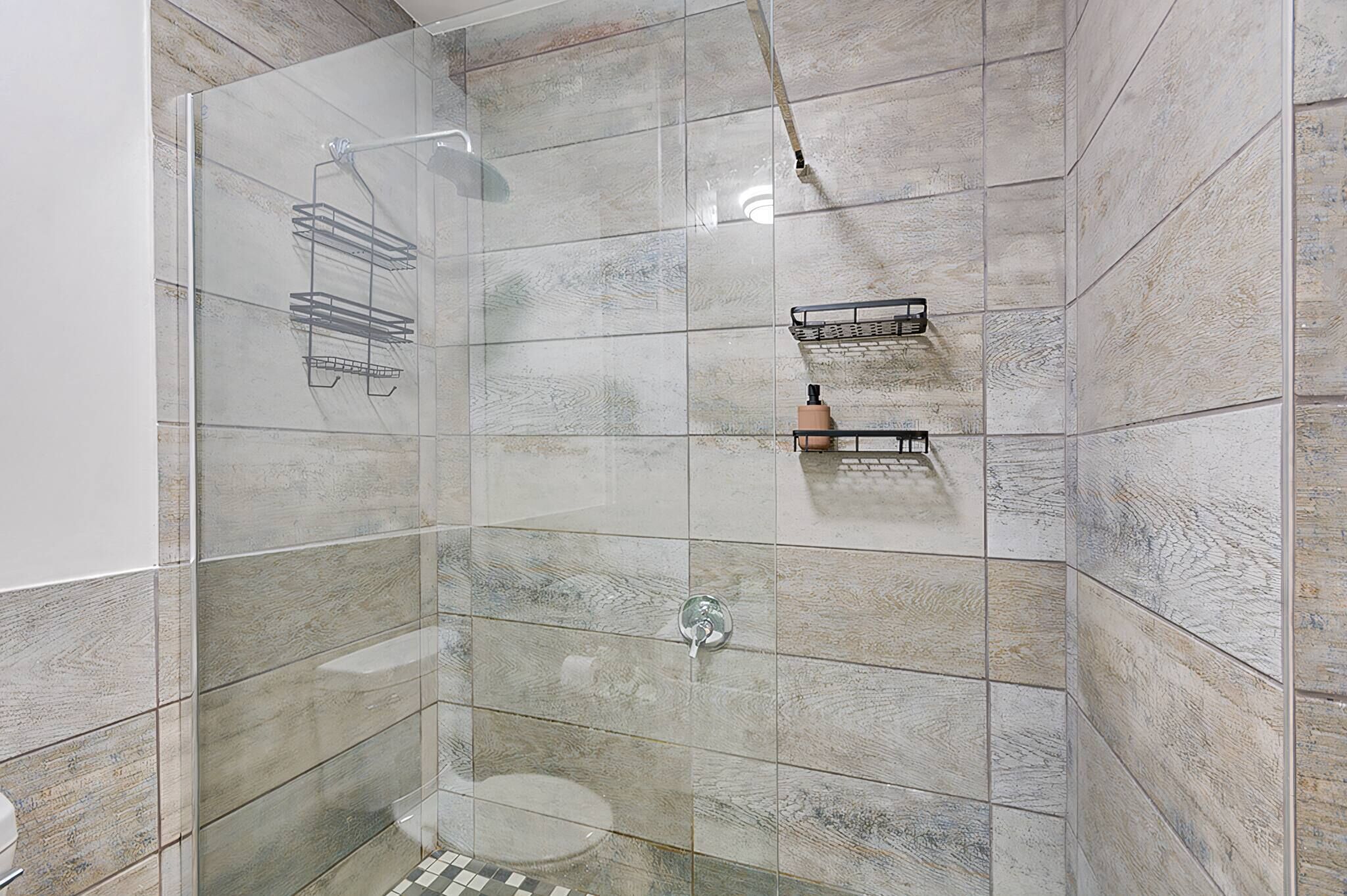 A shower with a glass door, tiled walls, and a metal rack.