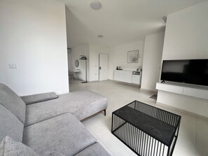 A modern living room with a grey sectional sofa, a black marble coffee table, and a flat-screen TV mounted on the wall.