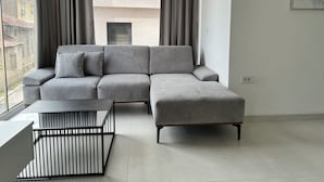 A modern living room with a grey sectional sofa, a black coffee table, and a view of buildings through large windows.