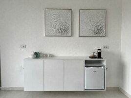 A kitchenette with a white cabinet, a small refrigerator, and two framed abstract wall art pieces.