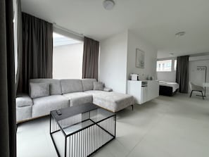 A modern living room with a grey sectional sofa, a glass coffee table, a white desk, and a chair.