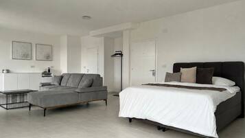 A modern bedroom with a bed, a grey sofa, a small table, and a floor lamp.