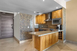 A modern kitchen with wooden cabinets, a granite countertop, a stainless steel microwave, and a patterned backsplash. - Luxury Beach Condo with Resort Access Vidanta (Nuevo Vallarta)