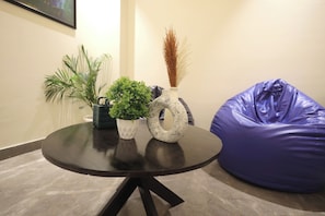 A round table with a vase and a potted plant, a bean bag chair, and a wall-mounted mirror. - ZEALIN Stays Golf Course Road PHASE 1 (Gurugram)
