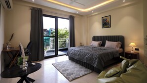 Ein Schlafzimmer mit einem Bett, einem Schreibtisch, einem Stuhl, einem Standventilator, einem Fenster mit Vorhängen und einem Balkon.