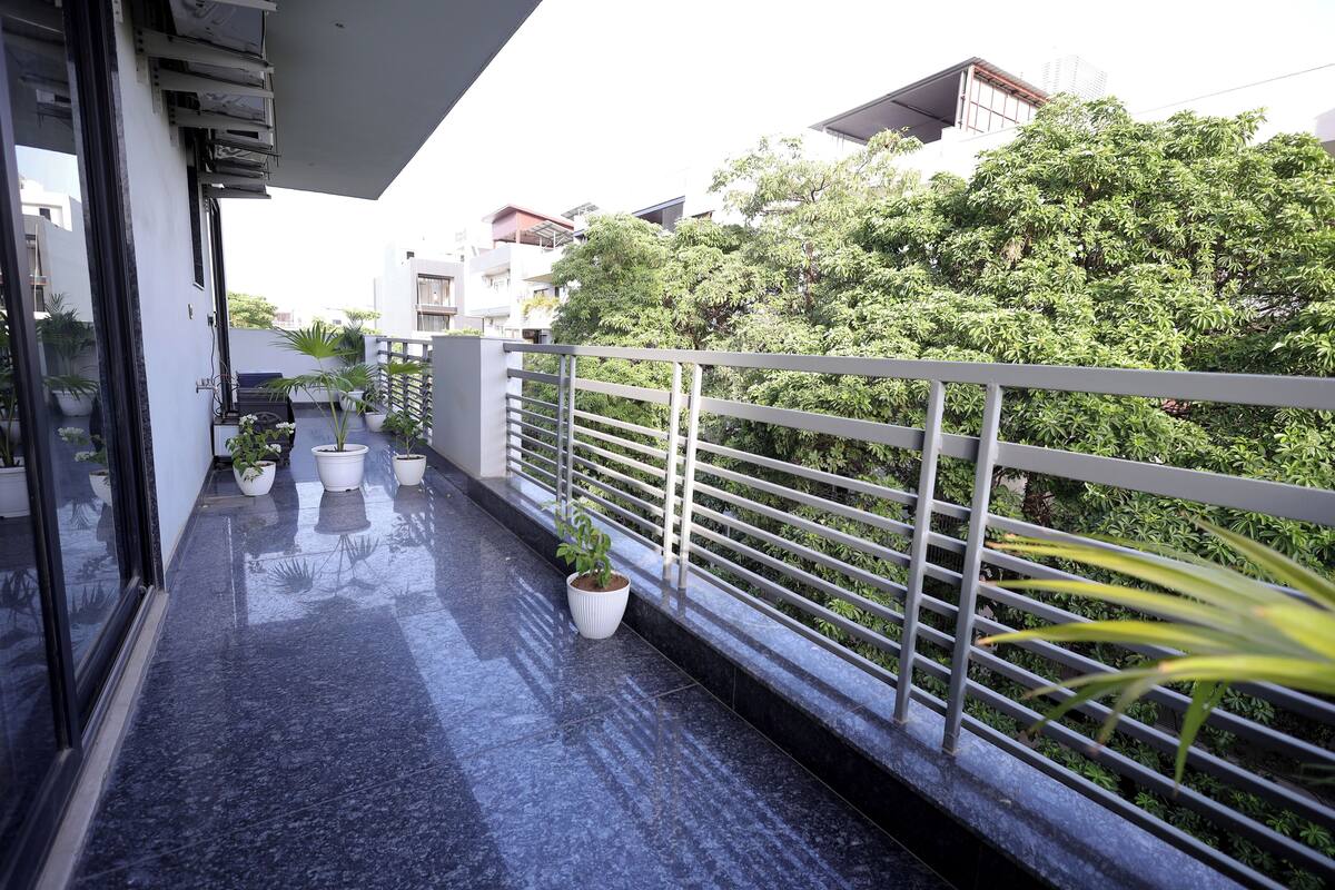 A balcony with potted plants, a metal railing, and a view of greenery and buildings.