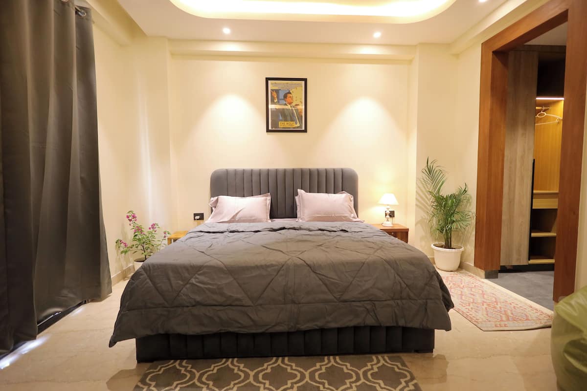 Quarto com uma cama grande, mesa de cabeceira, planta em vaso e porta que dá para outro cômodo.