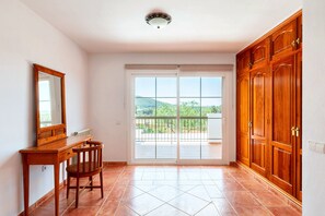Ein Zimmer mit einem Holztisch, Stuhl und einer großen Schiebeglastür, die auf einen Balkon mit Blick ins Grüne führt.
