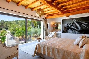 Ein Schlafzimmer mit einem großen Bett, Blick auf einen Garten und einer Holzbalkendecke.