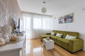 Ein modernes Wohnzimmer mit einem grünen Sofa, einem weißen Couchtisch und einer Büste auf einer weißen Konsole.
