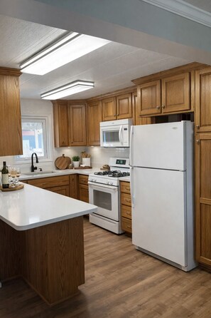 A kitchen with wooden cabinets, a white refrigerator, a microwave, an oven, and a sink. - Flint Hills Country Escape - Dog and Horse friendly (Maple Hill)