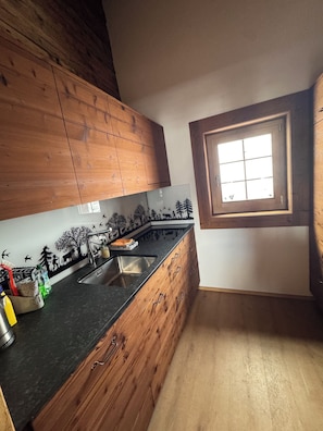 Une cuisine avec des meubles de rangement en bois, un plan de travail noir, une fenêtre et une fresque murale.