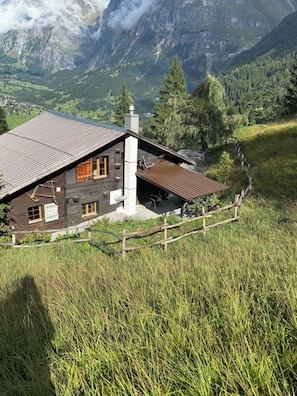 Une cabane rustique en bois, dotée d’un toit en pente, d’une cheminée et d’une clôture en bois, située dans une région montagneuse.