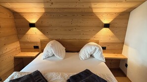 Habitación de una cabaña de madera con una cama, dos mesitas de noche y dos luces fijadas a la pared.