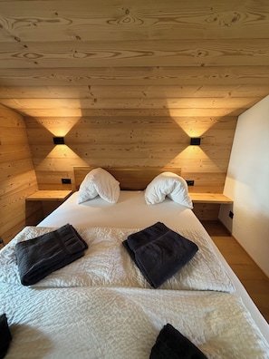 A wooden cabin room with a bed, two nightstands, and two wall-mounted lights.