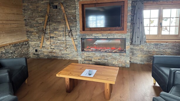 Una sala de estar con pared de piedra, vigas de madera, chimenea, televisor y dos sofás.