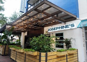 Ein Restaurant namens 'JOSEPHINE'S' mit überdachter Außenbestuhlung, hölzernen Pflanzgefäßen mit Grünpflanzen und moderner Architektur.