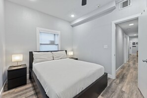 Un dormitorio moderno con cama, mesitas de noche, una ventana y un pasillo.