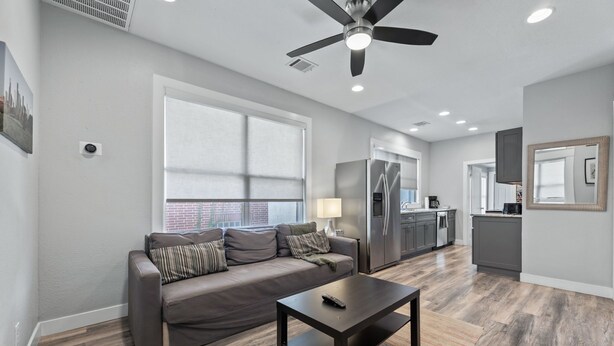 A modern living room with a sofa, coffee table, and a ceiling fan. - Entire Midtown 4plex - Gated Parking - Rail to NRG (Houston)