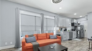 A modern living room with a sofa, a coffee table, and a kitchen in the background. - Entire Midtown 4plex - Gated Parking - Rail to NRG (Houston)