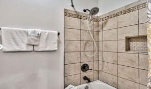 Une salle de bain équipée d’une baignoire, d’une douche avec un pommeau de douche amovible et d’un porte-serviettes avec des serviettes pliées.
